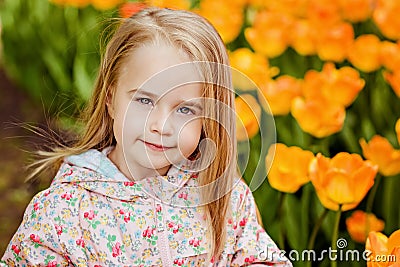 portrait of a very cute pretty girls blonde in a pink cloak around flower beds with red tulips in the Park Stock Photo