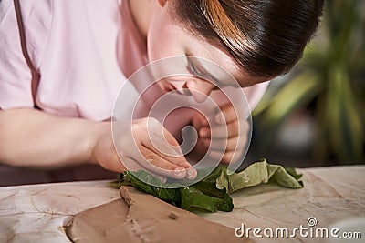 Woman touching with the finger fresh leaf while imprinting texture of it to the clay Stock Photo