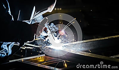 Portrait view of professional mask protected welder. Bright electric torch burns iron piece Stock Photo