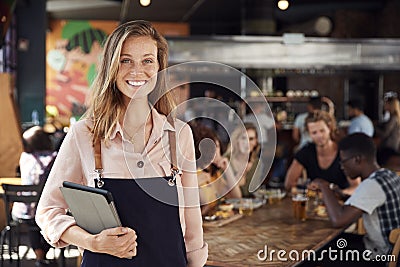 Portrait Of Waitress Holding Menus Serving In Busy Bar Restaurant Stock Photo