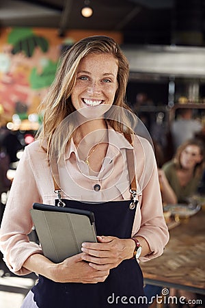 Portrait Of Waitress Holding Menus Serving In Busy Bar Restaurant Stock Photo