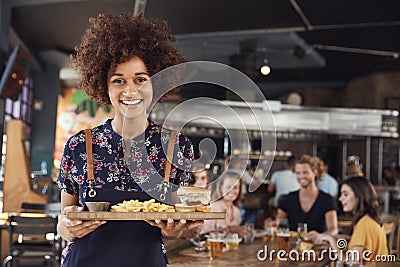 Portrait Of Waitress Serving Food To Customers In Busy Bar Restaurant Stock Photo