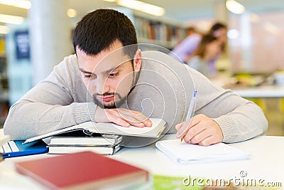 Portrait of upset adult man with stack of books on table in room of public library Stock Photo