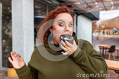 Portrait of a well-fed surprised woman eating a shocking chocolate donut. The concept of diet and obesity Stock Photo