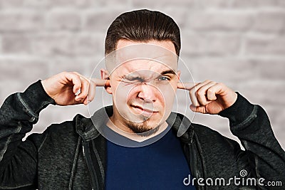 Portrait White man closes the ears in blue shirt on brick wall background Stock Photo