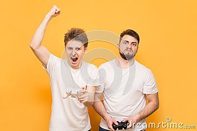 The portrait of the winner and losers are with joysticks in their hands on a yellow background. Two emotional men play video games Stock Photo