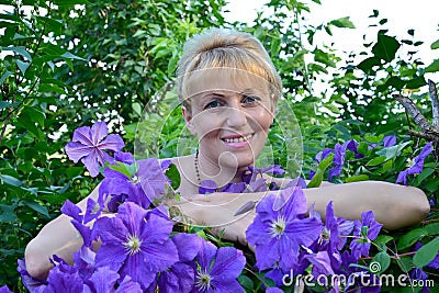 Portrait of the woman of average years among flowers Clematis Stock Photo