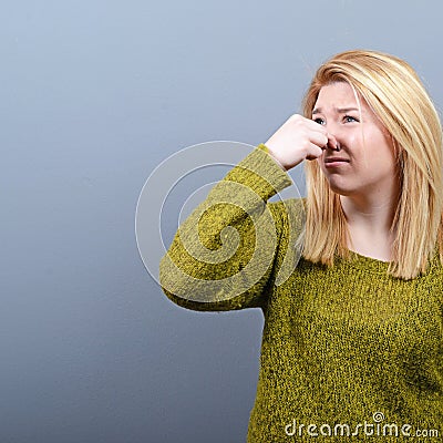 Portrait of woman covering nose with hand showing that something stinks against gray background Stock Photo