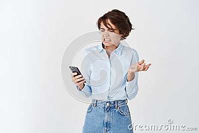Portrait of woman cringe and look with disgust at mobile screen, reading something disgusting, stare with aversion Stock Photo