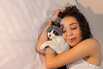 Portrait of woman with curly hair sleeping with her black and white cat in bed. Concept of love to animals, pets, care, Stock Photo