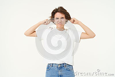 Portrait of woman disturbed by loud sound, shuts her ears, annoyed by music, frowning, standing over white background Stock Photo