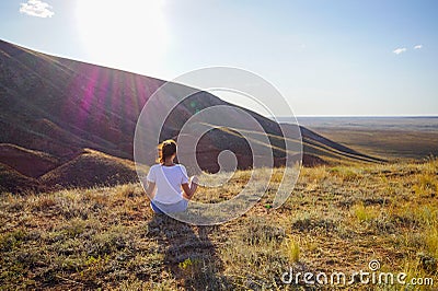 Portrait of a woman meditative practice sitting on the ground in the Lotus position and looking into the distance at the field, Stock Photo