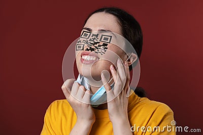 Portrait of a woman with a QR code instead of eyes and nose, removing protective mask from her new face. Brown Stock Photo