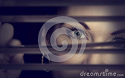 Portrait of a woman standing in darkness looking through blinds Stock Photo