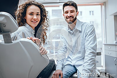 Portrait of a woman with toothy smile sitting at the dental chair with doctor on the background at the dental office Stock Photo