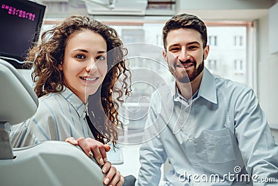 Portrait of a woman with toothy smile sitting at the dental chair with doctor on the background at the dental office Stock Photo