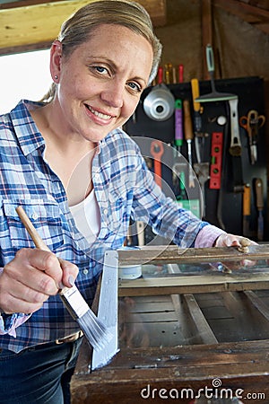 Portrait Of Mature Woman Upcycling Furniture In Workshop At Home Painting Cabinet Stock Photo