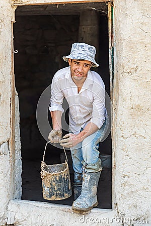 Portrait of a worker applying mud plaster to a traditional stone house Editorial Stock Photo