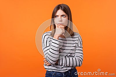 Portrait of worried frustrated woman with brown hair in long sleeve striped shirt. indoor studio shot on orange Stock Photo