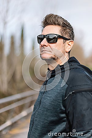 Portrait of a 45-50 years old man with sport clothes, sunglasses and toupee in exterior. Concept of relaxation after sports, Stock Photo