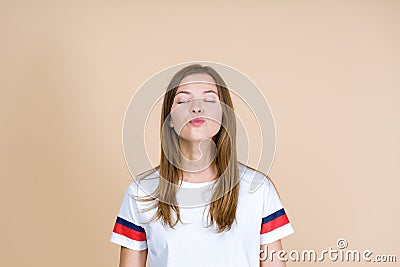 Portrait of young adult woman waiting kiss while standing isolated on pastel beige background Stock Photo