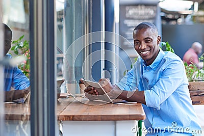 Smiling African man working online at a sidewalk cafe counter Stock Photo