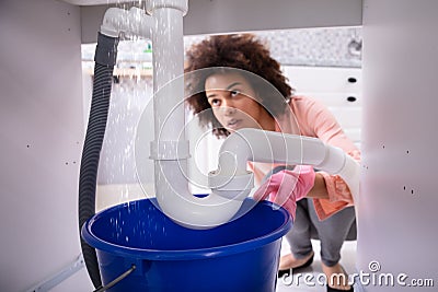 Woman Looking At Water Leaking From Sink Pipe Stock Photo