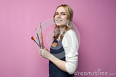 Portrait of young artist, girl holds brushes and smiles on a pink background, student of art school, profession of an artist Stock Photo