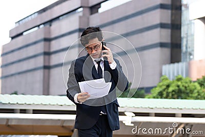 Portrait young Asian business man in suit analyzing charts or paperwork in hands outdoors Stock Photo