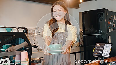 Portrait young Asian lady barista waitress holding coffee cup feeling happy at urban cafe. Asia small business owner girl in apron Stock Photo