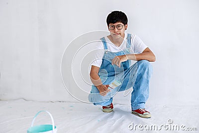 Portrait young asian man in white shirt with bear suit sit and painted plot on hand and look at camera in white wall, renovation Stock Photo