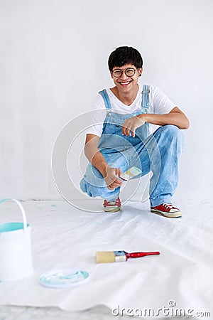 Portrait young asian man in white shirt with bear suit sit and painted plot on hand and look at camera in white wall, renovation Stock Photo