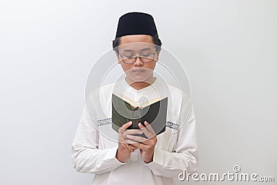 young Asian muslim man reading and reciting Holy book of Quran seriously. Isolated image on white background Stock Photo