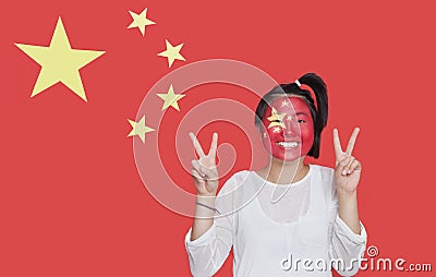 Portrait of young Asian woman with painted face gesturing peace sign against Chinese flag Stock Photo