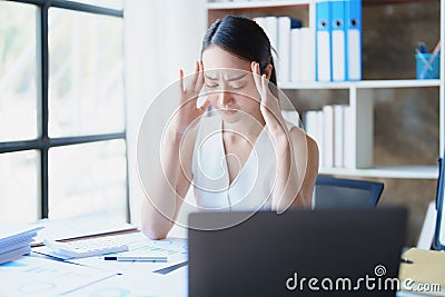 Portrait of a young Asian woman showing acute headache from sitting for a long time at work. Stock Photo