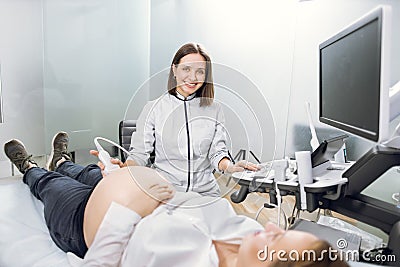 Portrait of young attractive female doctor, posing to camera with smile while conducting ultrasound scanning procedure Stock Photo
