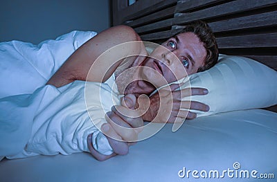 Portrait of young attractive scared man in fear and panic suffering horror nightmare covering face with blanket sleepless at night Stock Photo