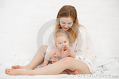 Portrait of young barefoot blond woman with little naked baby in white bedroom, after cleaning procedures. Mother caring Stock Photo