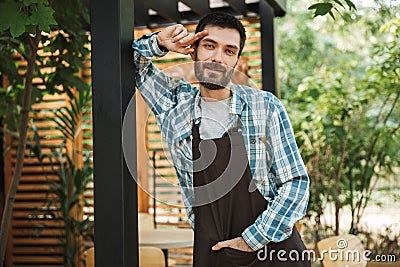 Portrait of young barista man smiling at camera while working in street cafe or coffeehouse outdoor Stock Photo