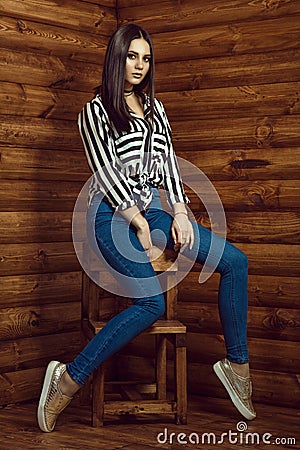 Portrait of young beautiful dark-haired model wearing skinny high-waisted jeans, striped shirt, choker and golden sneakers Stock Photo