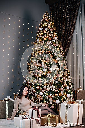 portrait of a young, beautiful girl in a dress near the Christmas tree with a bunch of gifts Stock Photo