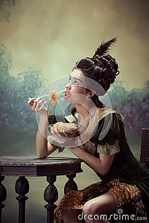 Portrait of young beautiful girl , princess in retro dress eating noodles with dreamy face against dark vintage Stock Photo