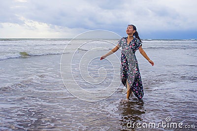 Portrait of young beautiful and happy Asian Chinese woman on her 20s or 30s wearing long chic dress walking alone on beach sea Stock Photo