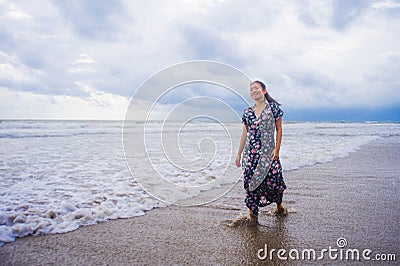 Portrait of young beautiful and happy Asian Chinese woman on her 20s or 30s wearing long chic dress walking alone on beach sea Stock Photo