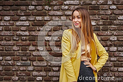 Portrait of a young beautiful laughing woman with long hair and a yellow jacket against the background of a brick wall on a cloud Stock Photo