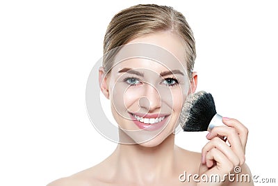 Portrait of a young blond woman applying dry cosmetic tonal foundation on her face using make up brush. Beauty portrait. Stock Photo