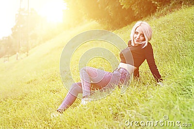 Portrait of a young blond woman with short hair sitting on a green field Stock Photo