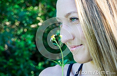 Cute close profile portrait of young blond woman face smiling with blue clear eyes and a daisy flower isolated in nature Stock Photo