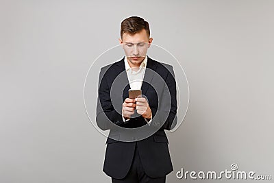 Portrait of young business man in classic black suit, shirt using mobile phone typing sms message isolated on grey Stock Photo