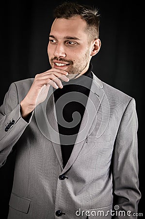 Portrait of a young businessman in a gray suit holding his chin with his fingers and seems to hesitate while he is pondering Stock Photo